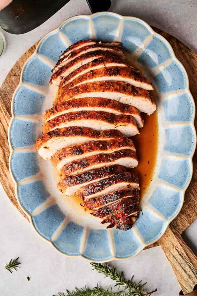 Sliced roasted turkey breast on a blue oval platter with visible herbs and juices.