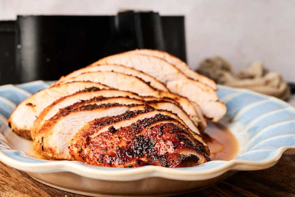 Sliced roasted meat on a blue and white plate with a textured pattern, set on a wooden surface.