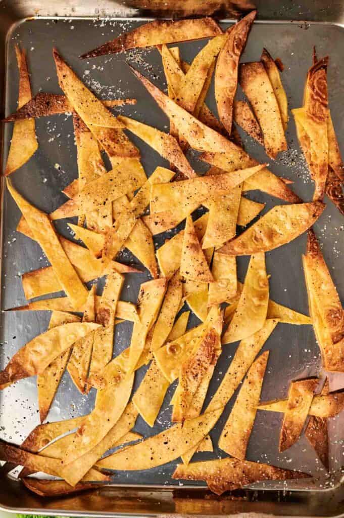 A baking sheet with crispy, golden-brown tortilla chip strips sprinkled with salt and pepper, perfect for topping a hearty bowl of chicken tortilla soup.