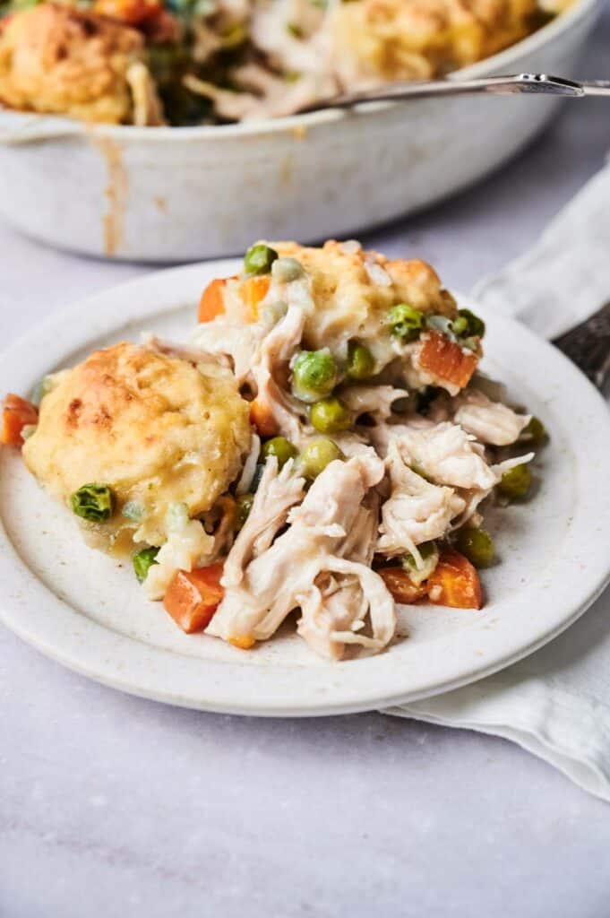 Plate of Air Fryer Chicken and Dumpling Casserole with golden biscuits on top, featuring peas and carrots, set on a white dish. Baking dish in the background.
