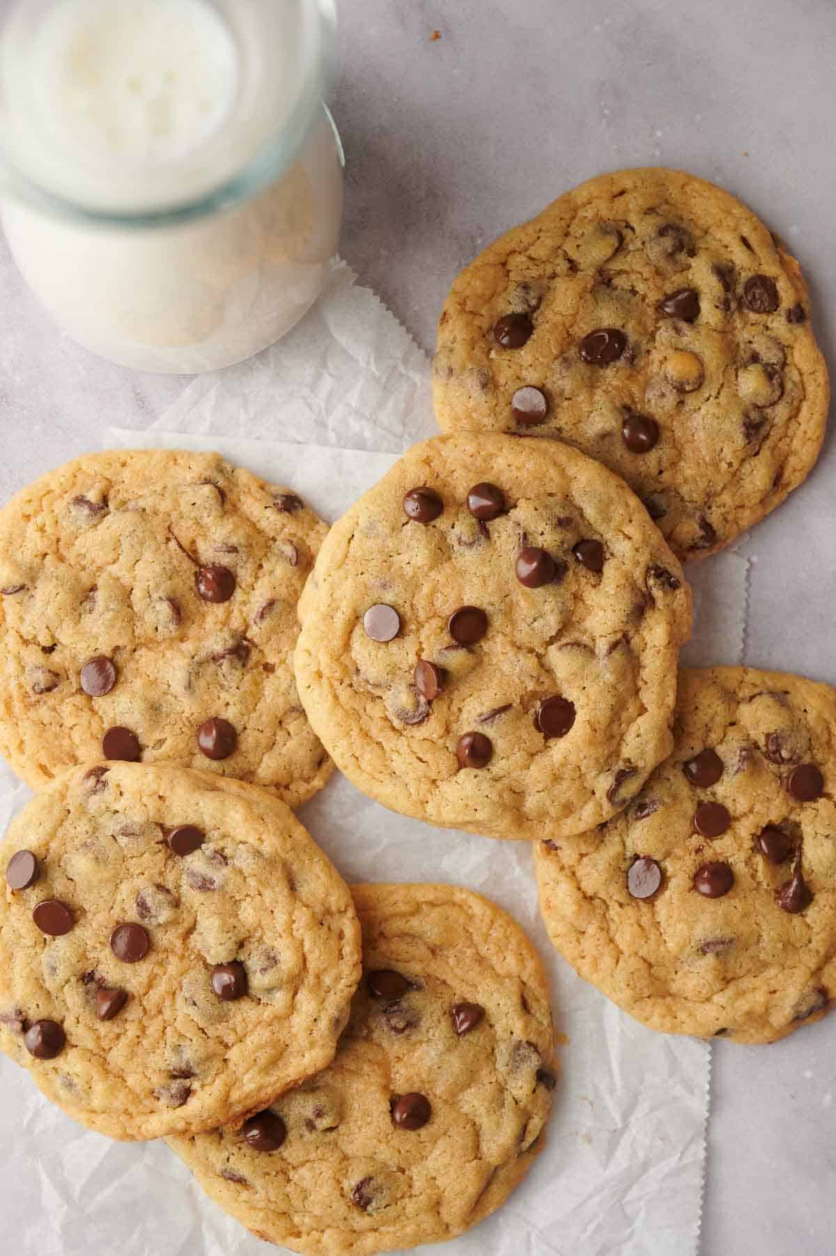 Chocolate chip cookies arranged on parchment paper next to a bottle of milk.