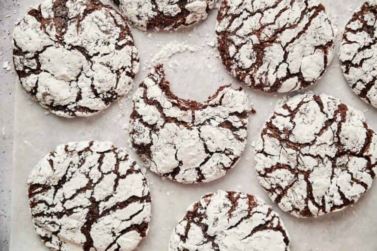Chocolate crinkle cookies covered in powdered sugar on a baking sheet. One cookie is partially eaten.