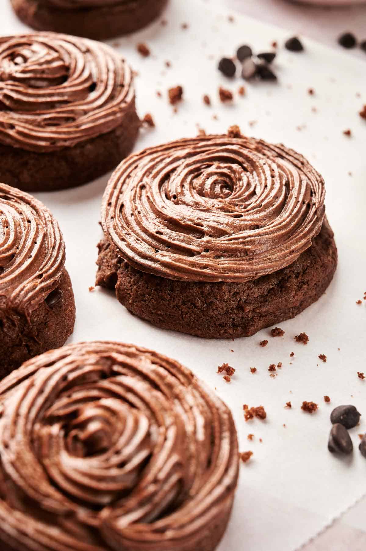 Close-up of Copycat Crumbl Chocolate Cake Cookies featuring swirled chocolate frosting, nestled on parchment paper with scattered chocolate chips.
