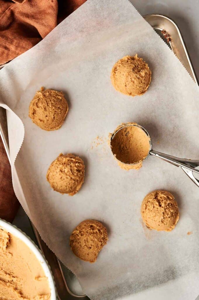Cookie dough scoops on parchment paper with a cookie scoop, ready for baking.