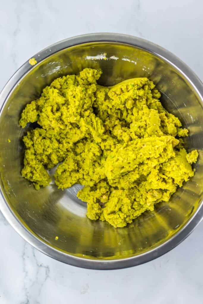 A stainless steel bowl filled with a greenish-yellow, crumbly mixture, perfect for crafting spooky Halloween eyeballs.