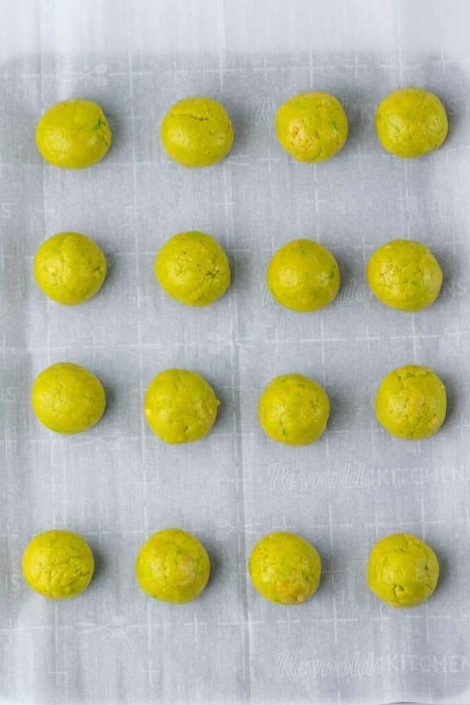 Fifteen round, yellow dough balls, resembling spooky Halloween eyeballs, are evenly spaced on a parchment-lined baking sheet.