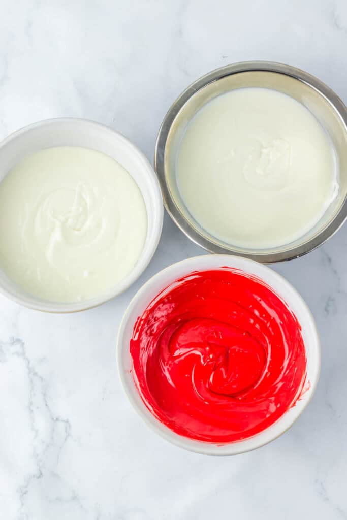 Three bowls filled with melted candy: two with white candy melts and one with red candy melts, placed on a marble surface, perfect for crafting spooky Halloween eyeballs.