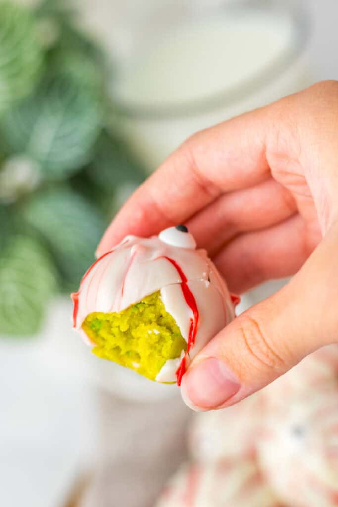 A hand holding a bite-marked treat with a green interior and white, red-streaked exterior, resembling spooky Halloween eyeballs.