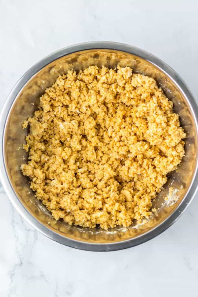 A stainless steel bowl containing crumbled mixture, likely a dough or a grain-based substance, on a white marble surface with spooky Halloween eyeballs scattered around.