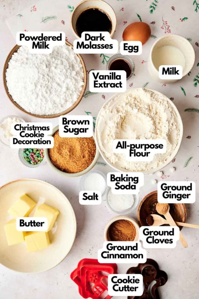 Ingredients for baking are laid out, including flour, brown sugar, baking soda, spices, powdered milk, butter, egg, molasses, vanilla extract, milk, cookie cutter, and decorations.