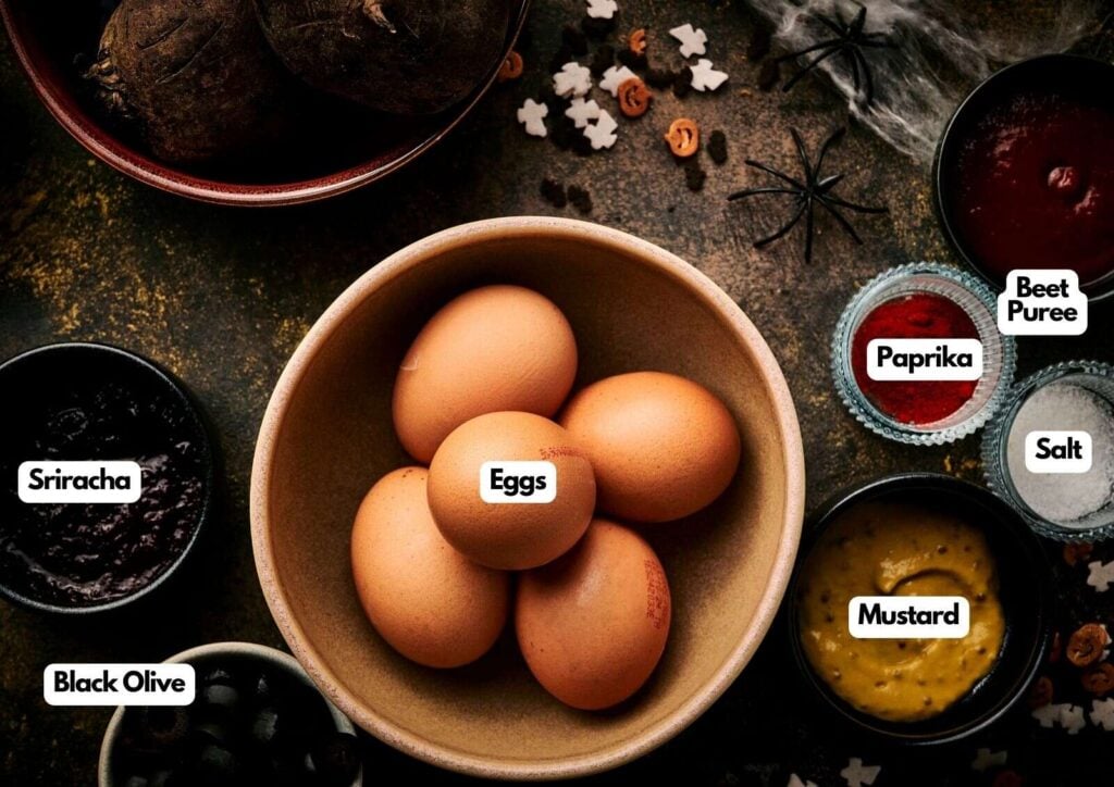 A bowl of eggs surrounded by labeled bowls containing black olive, sriracha, beet puree, paprika, salt, and mustard on a dark surface—perfect ingredients for making spooky Halloween deviled eggs with festive decorative elements.