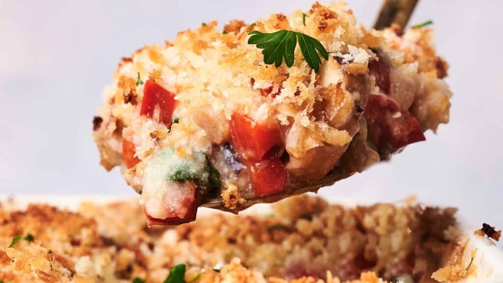 A spoonful of vegetable casserole topped with golden breadcrumbs and garnished with a parsley leaf.