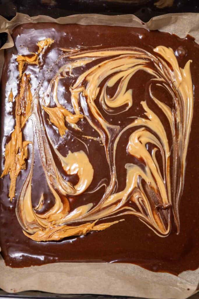 A luscious blend of swirled chocolate and peanut butter nestled on parchment paper in a baking pan, creating the perfect Peanut Butter Brownies.