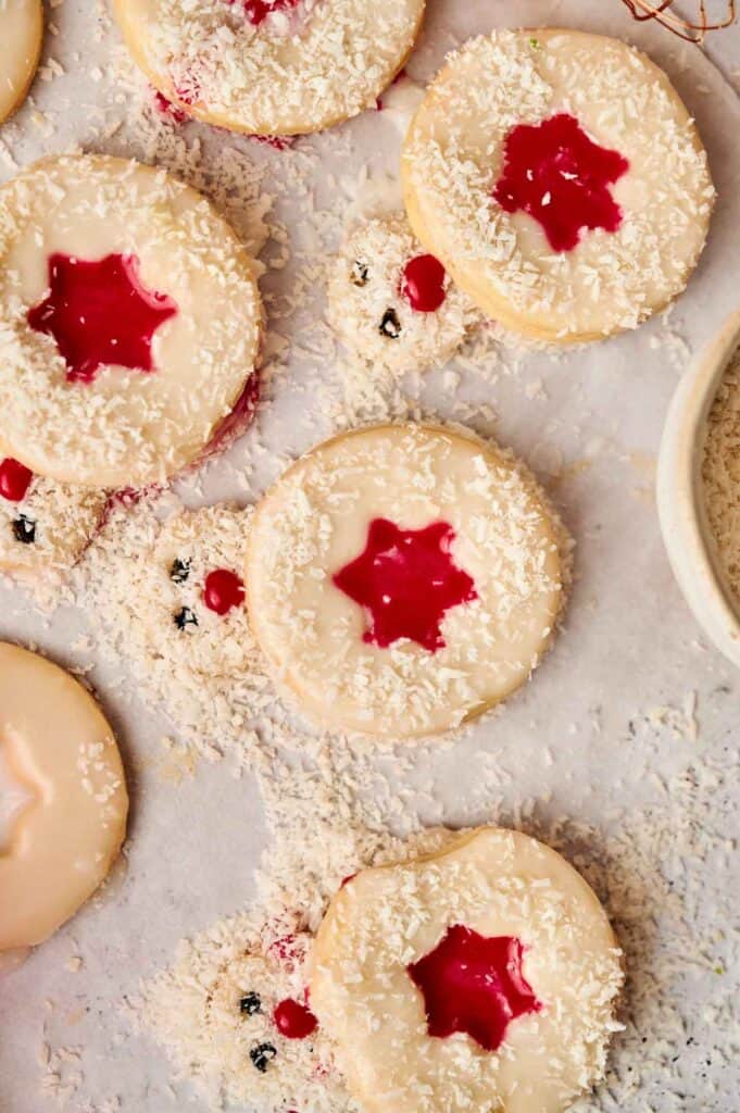 Round cookies with star-shaped raspberry jam centers are sprinkled with shredded coconut on a parchment paper background.