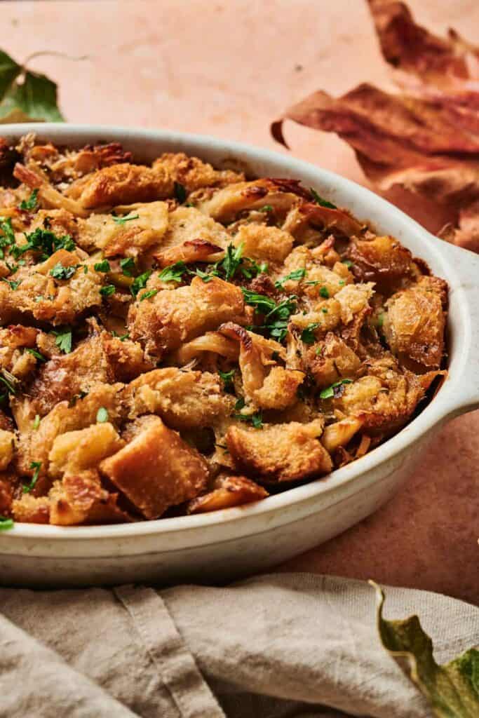A Thanksgiving casserole with crispy bread stuffing, garnished with chopped herbs in a white ceramic baking dish on a textured surface, reminiscent of an air fryer&rsquo;s perfect touch, surrounded by fallen leaves.