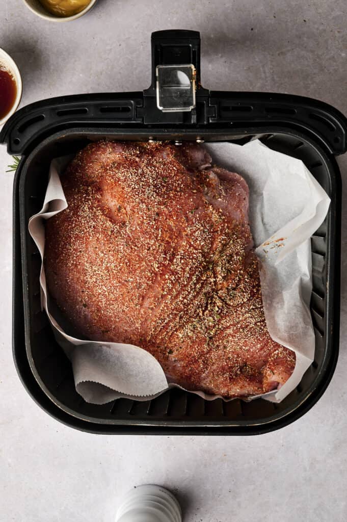 Seasoned raw meat placed on parchment paper in an air fryer basket, ready for cooking.
