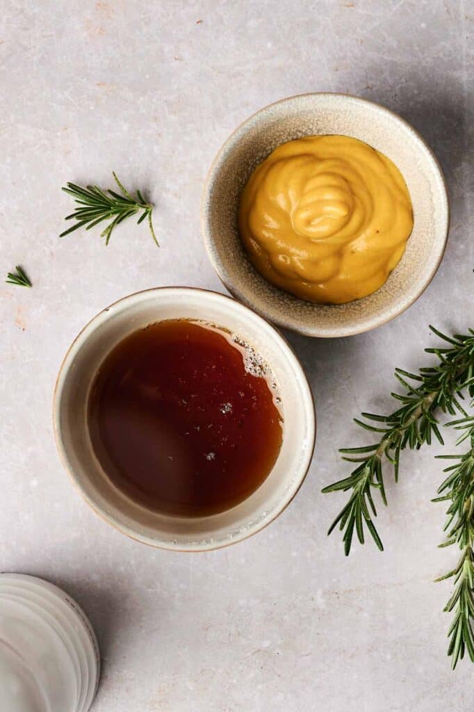 Two bowls on a table: one with mustard, the other with dark sauce, perfectly paired for turkey breast. Sprigs of rosemary are scattered nearby.