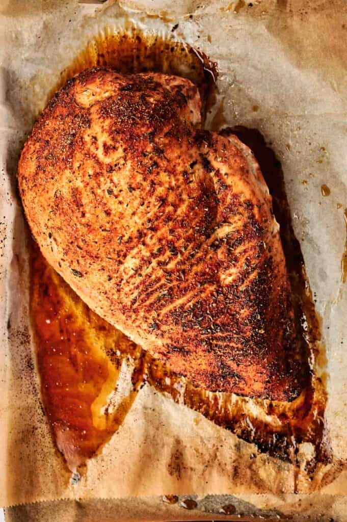Roasted seasoned turkey breast on parchment paper with visible juices.