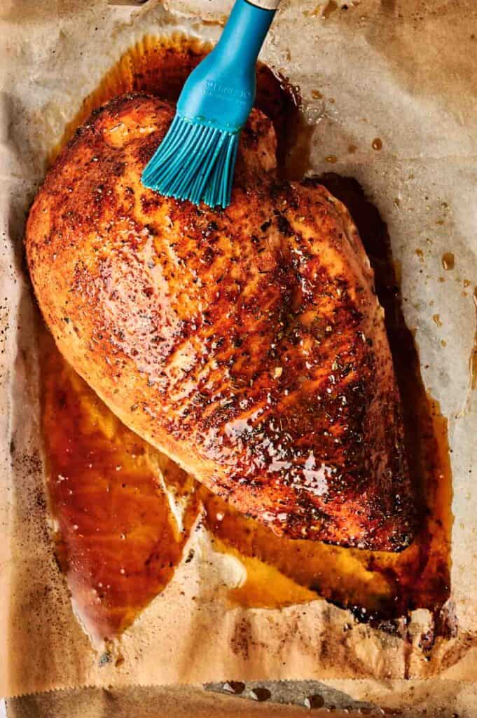 A perfectly cooked turkey breast is delicately brushed with a rich glaze, resting invitingly on parchment paper.