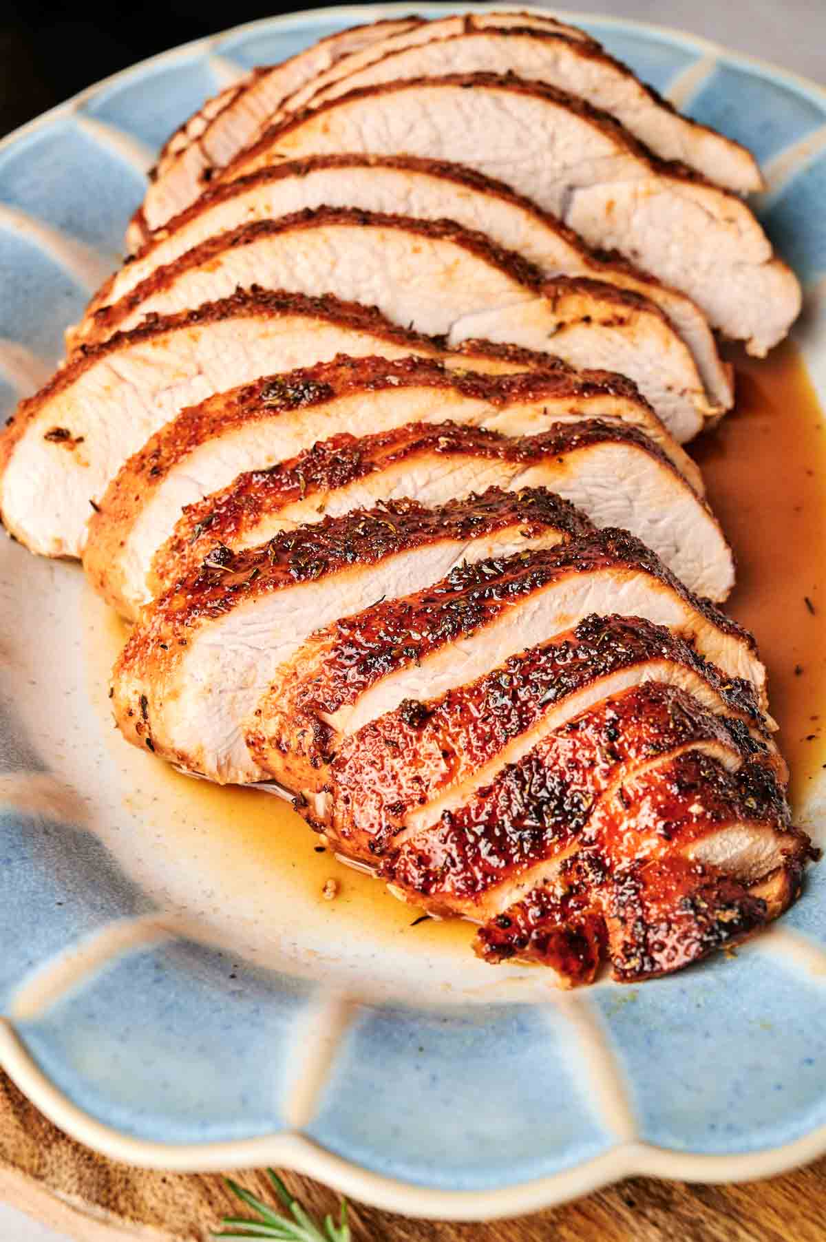 Sliced turkey breast is meticulously arranged on a blue plate, glistening with savory juices.