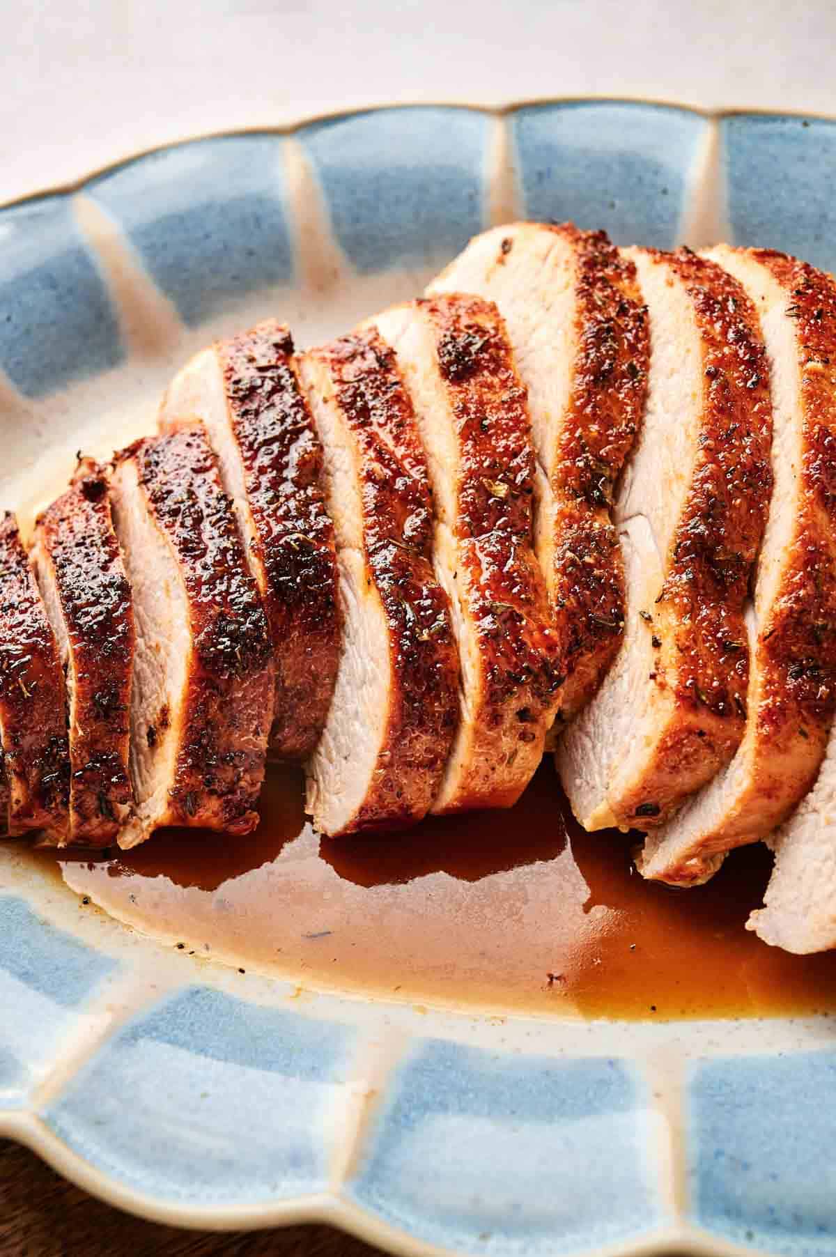 Sliced roasted chicken breast on a blue plate, with visible seasoning and juices pooling at the bottom.