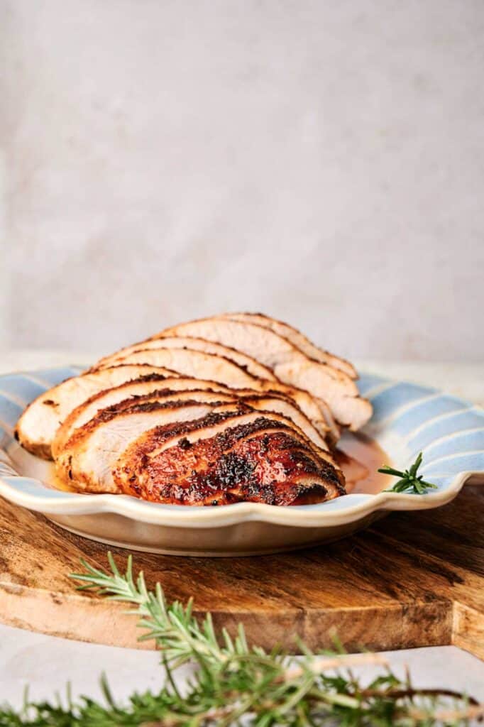 Sliced roasted turkey breast is elegantly arranged on a decorative plate, complemented by a fragrant rosemary garnish.