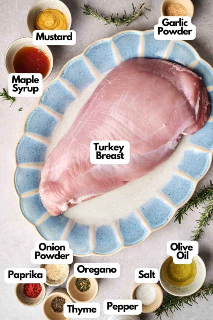 Raw turkey breast rests on a blue-rimmed plate, encircled by clearly labeled ingredients: mustard, maple syrup, garlic powder, onion powder, paprika, oregano, thyme, pepper, salt, and olive oil.