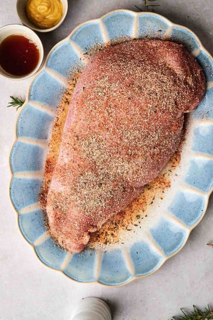 A seasoned turkey breast rests on a blue and white platter, accompanied by small bowls of mustard and sauce.