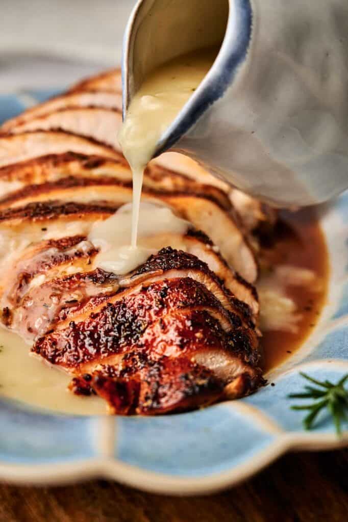 Sliced roasted meat on a blue plate with rich turkey gravy being poured over it from a white gravy boat.