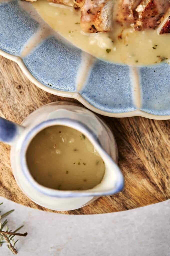 A blue plate with sliced meat and turkey gravy beside a ceramic gravy boat filled with more of the same savory sauce, all on a wooden surface.