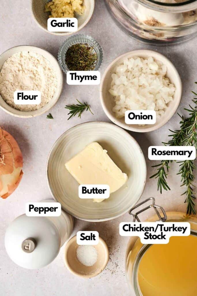 Ingredients laid out for turkey gravy: garlic, flour, thyme, chopped onion, rosemary, pepper, butter, salt, and a jar of chicken or turkey stock.