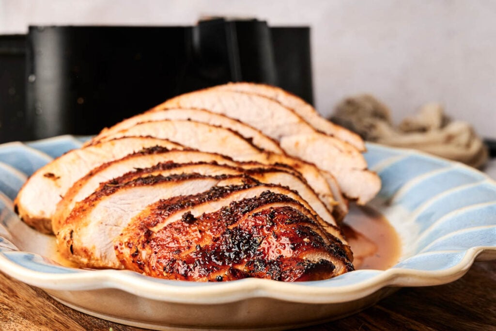 Air Fryer Turkey Breast, sliced and seasoned, arranged on a blue and beige plate with visible juices, set on a wooden surface.