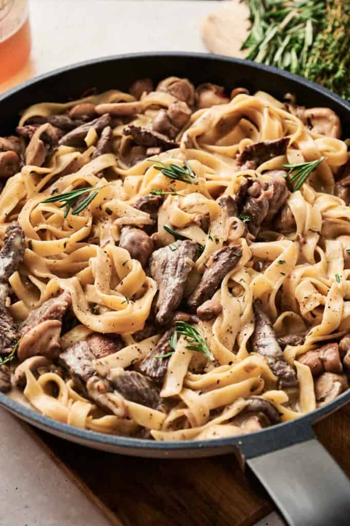 A pan of creamy beef and mushroom fettuccine, reminiscent of Beef Stroganoff, topped with aromatic rosemary sprigs.