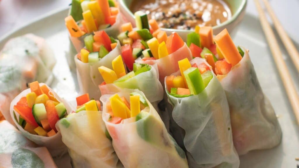 A plate of fresh vegetable spring rolls with a bowl of dipping sauce and chopsticks.