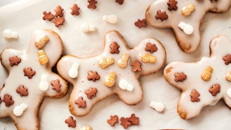 Gingerbread cookies with white icing are decorated with small, edible snowmen and gingerbread figures, arranged on a light surface.