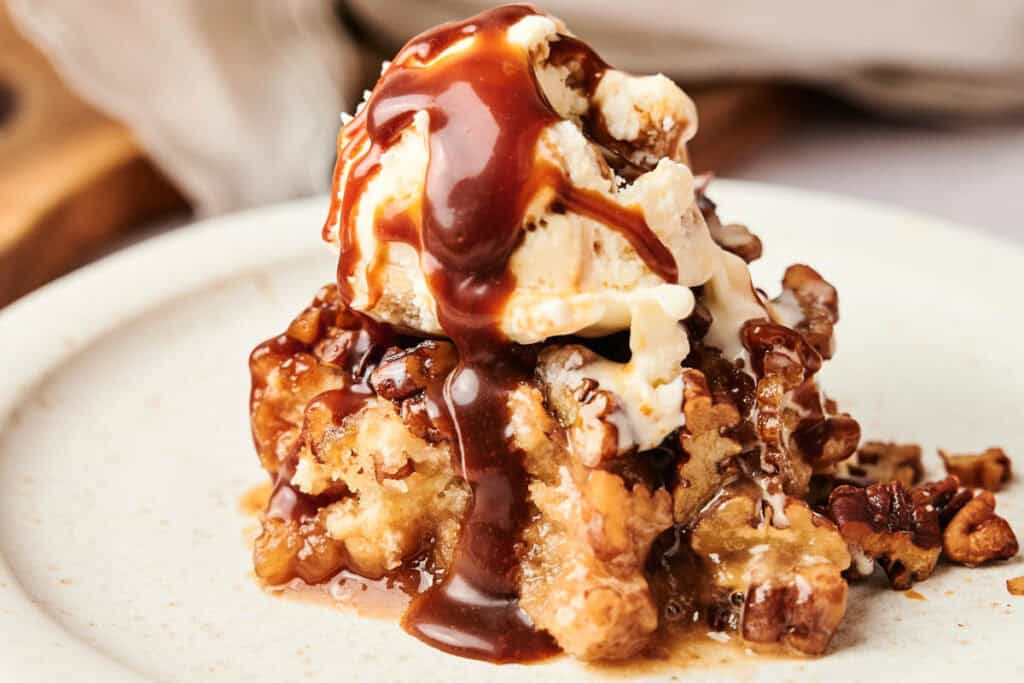 A dessert plate features a scoop of ice cream drizzled with chocolate sauce atop a warm air fryer pecan pie cobbler, garnished with nuts.
