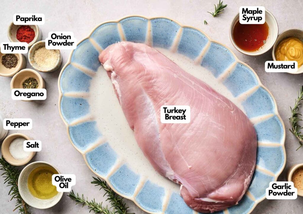 Ingredients for Air Fryer Turkey Breast: raw turkey breast on a blue platter surrounded by bowls of paprika, thyme, oregano, black pepper, salt, onion powder, garlic powder, olive oil, maple syrup, and mustard.