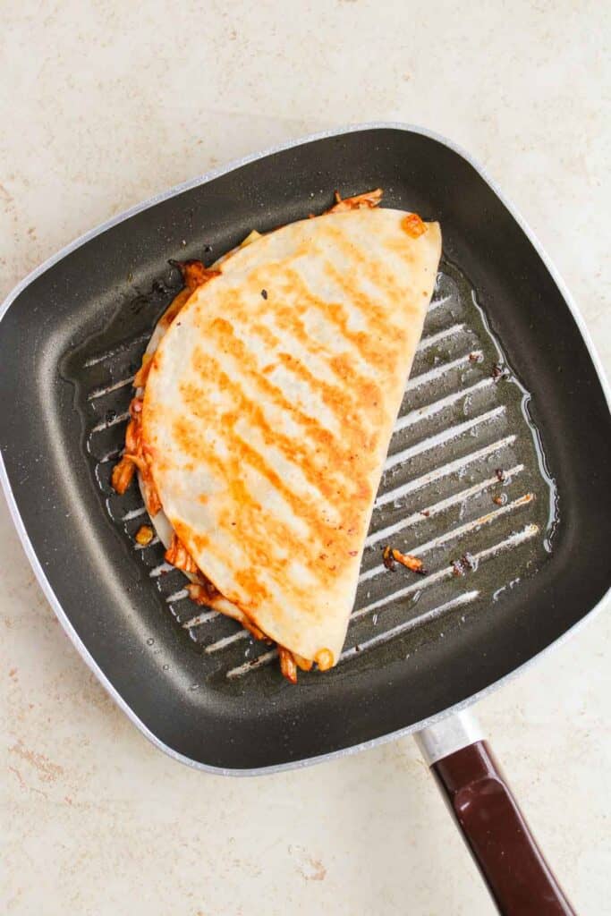 A BBQ chicken quesadilla sizzles on a grill pan, showing off its tantalizing golden grill marks.