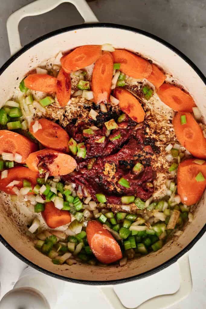 A pot with sautéed carrots, onions, and green peppers arranged around a central dollop of tomato paste on a stove.