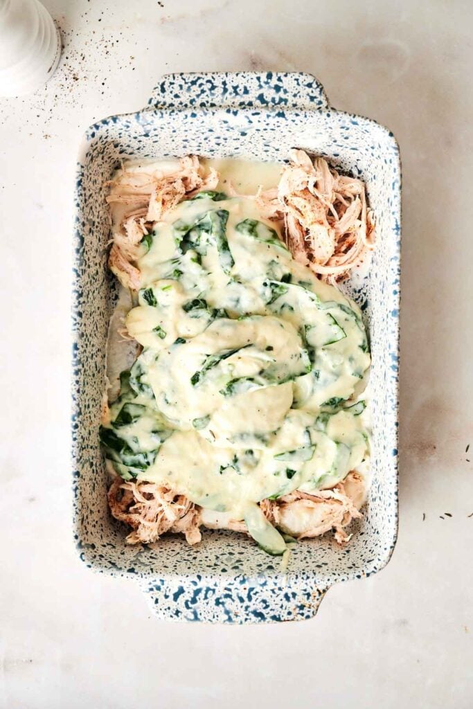 Shredded chicken in a speckled baking dish topped with a creamy spinach sauce