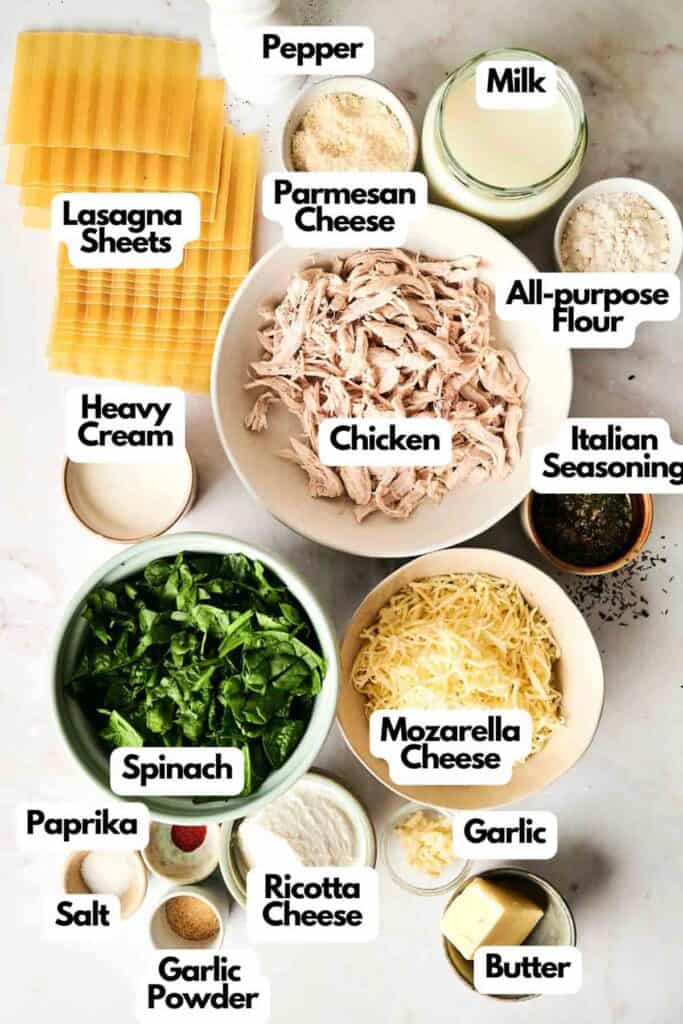 Ingredients for a creamy Chicken Alfredo lasagna are arranged on a surface, featuring juicy chicken, rich cheeses, fresh spinach, hearty lasagna sheets, aromatic spices, milk, smooth cream, fragrant garlic, butter, and flour.