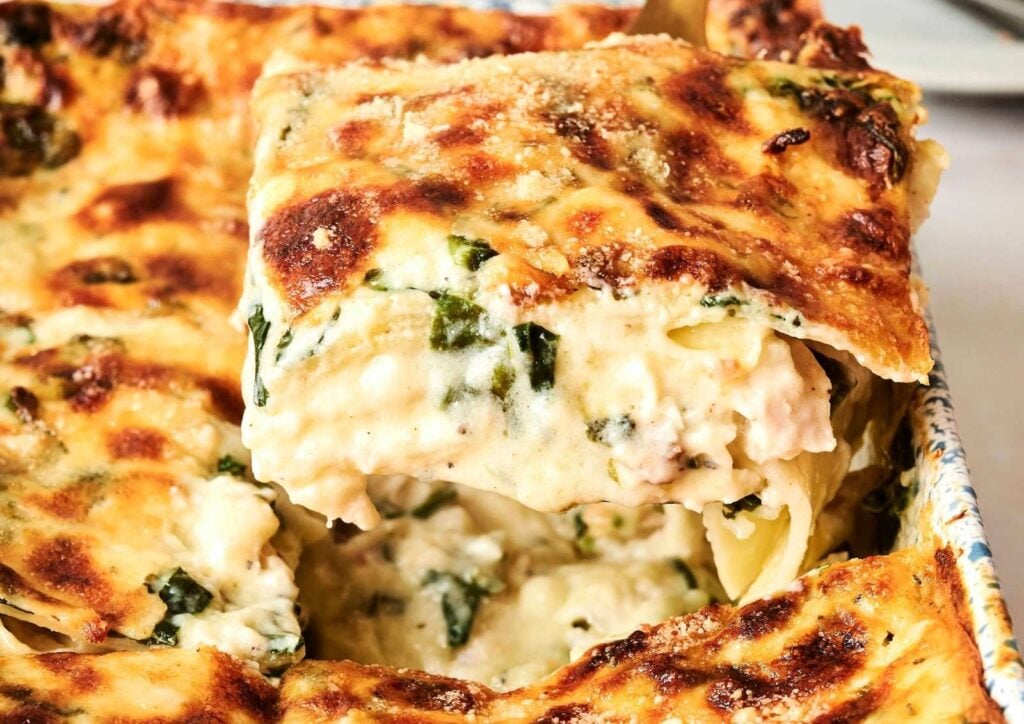 A serving of creamy Chicken Alfredo lasagna with spinach being lifted from a baking dish.