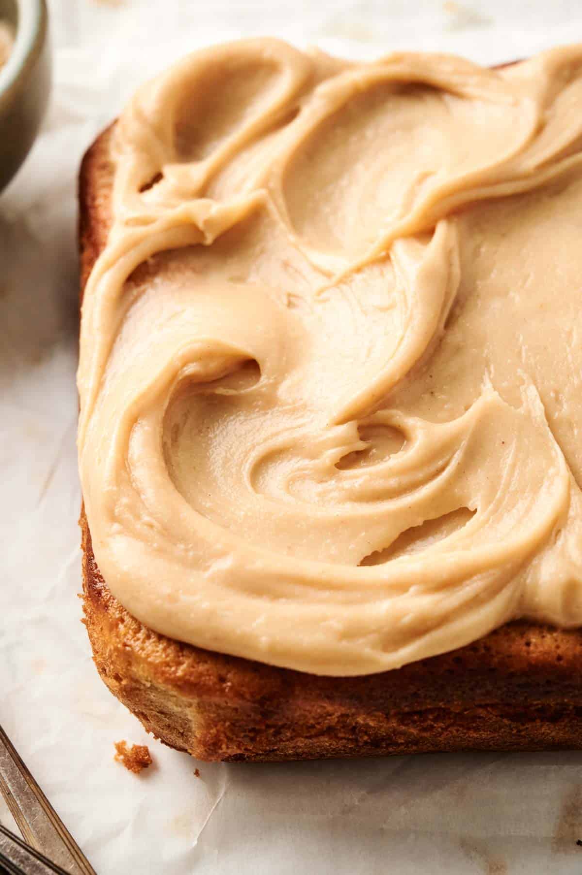 A Peanut Butter Cake with creamy, light brown frosting spread smoothly on top, set elegantly on parchment paper.