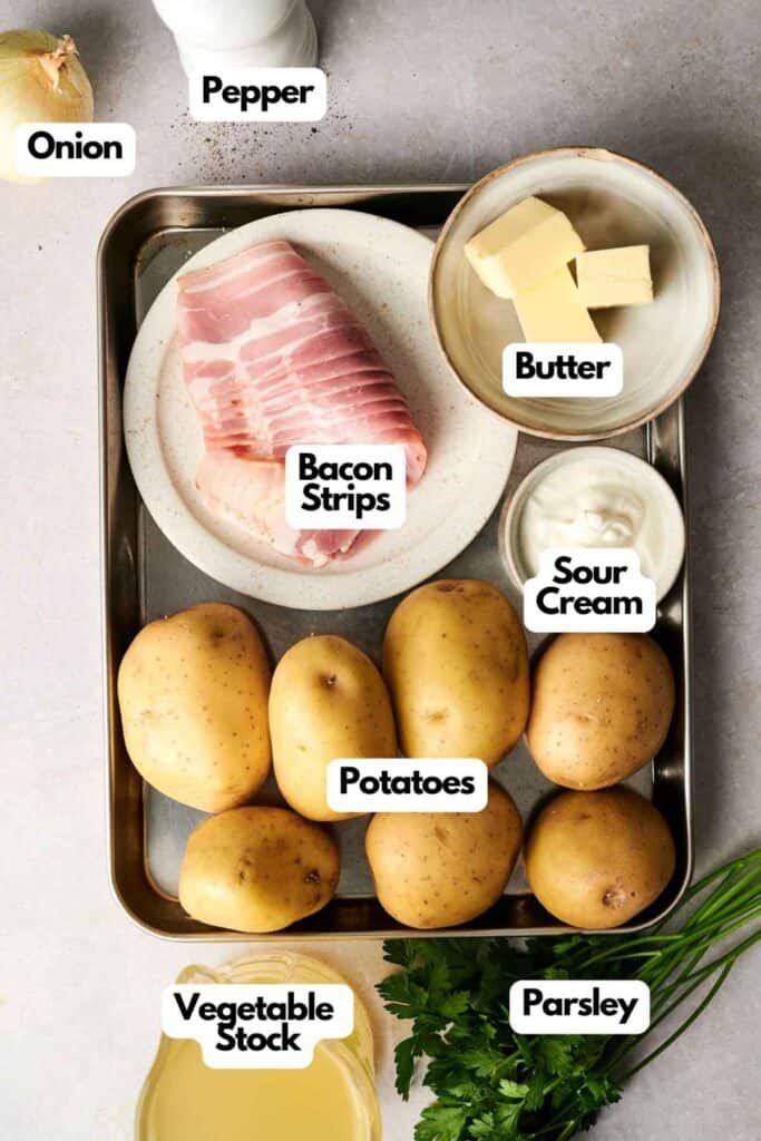 A tray brimming with potato soup essentials: creamy potatoes, crispy bacon strips, a dollop of butter, tangy sour cream, aromatic onion and pepper, rich vegetable stock, and fresh parsley.