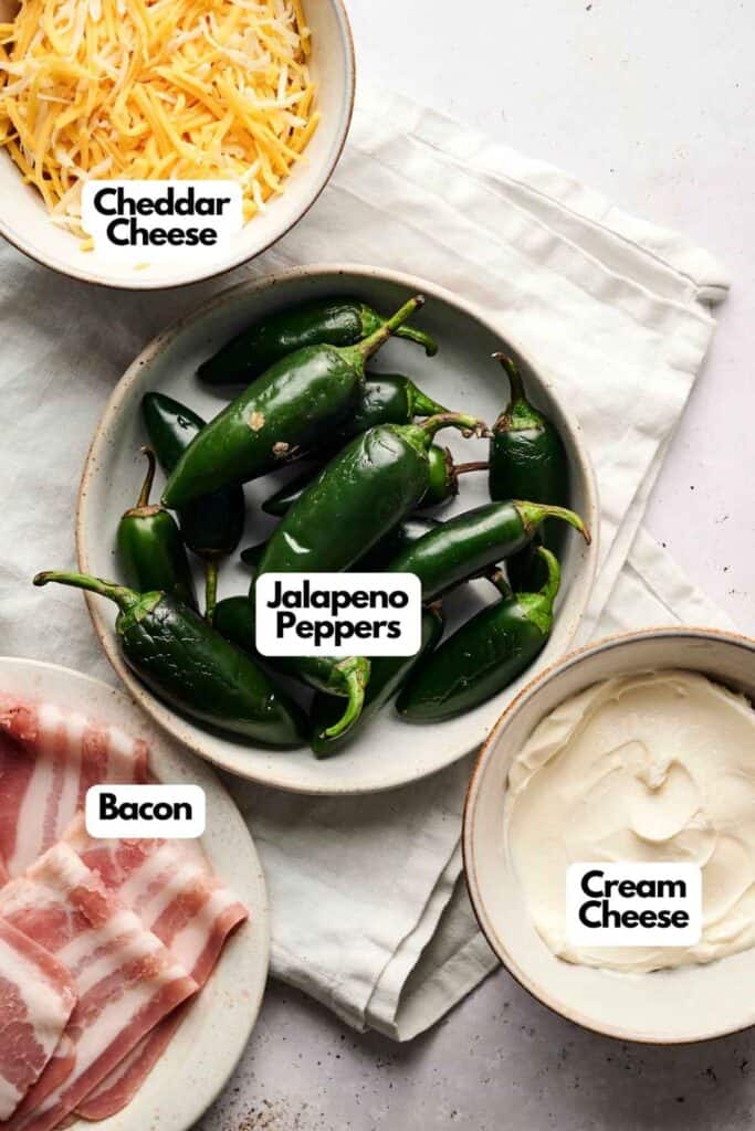 Bowls of cheddar cheese, bacon-wrapped jalape&ntilde;o poppers, and cream cheese strips are artfully arranged on a white cloth.