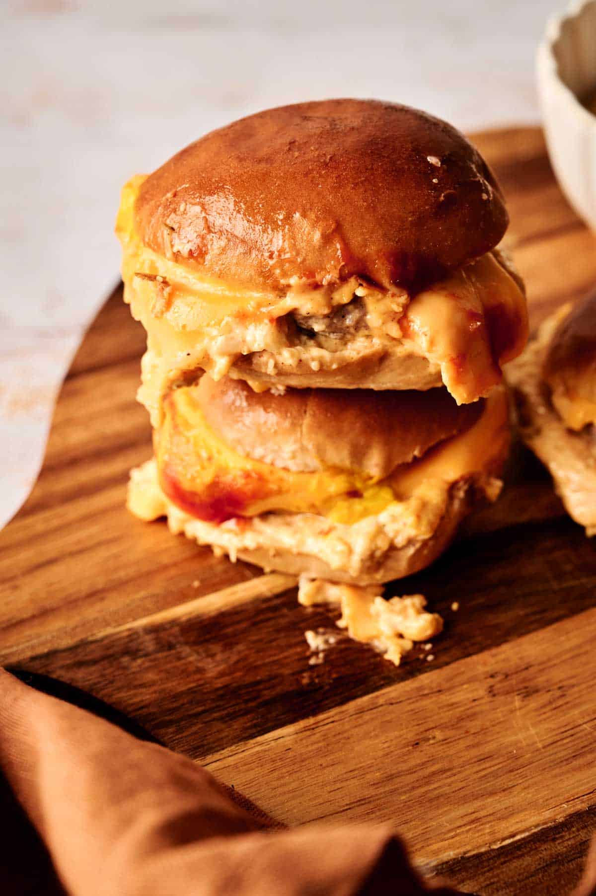 Two mouthwatering cheeseburger sliders, stacked high with melted cheese, sit enticingly on a wooden board.