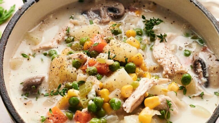 A bowl of creamy chicken stew with potatoes, peas, carrots, corn, mushrooms, and herbs.