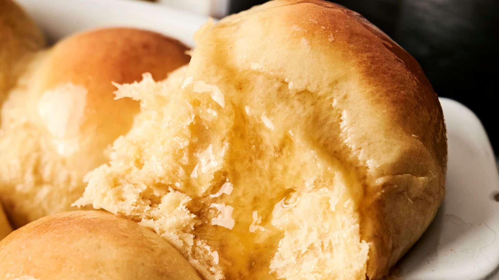 Close-up of freshly baked dinner rolls with a brushed glaze, arranged in a dish.