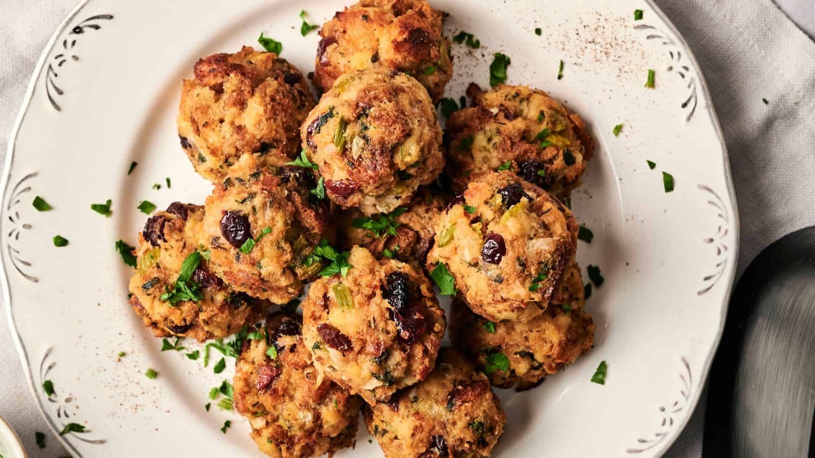 A plate of baked stuffing balls garnished with chopped herbs and cranberries.