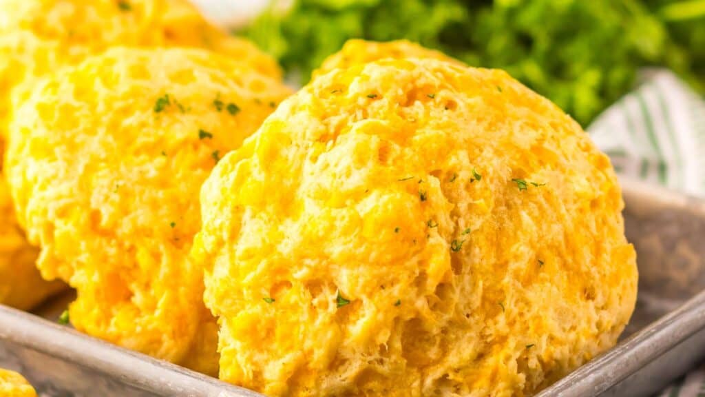 Close-up of freshly baked cheddar biscuits garnished with herbs on a baking tray.